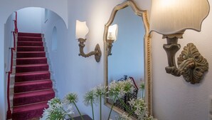 Un escalier recouvert d’une moquette rouge, un grand miroir décoratif, des appliques murales et des fleurs blanches.