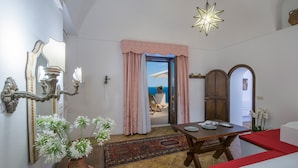 Une pièce comprenant une table à manger, des chaises, un canapé rouge, un miroir décoratif, un luminaire en forme d’étoile et une vue sur la mer, visible à travers une porte.