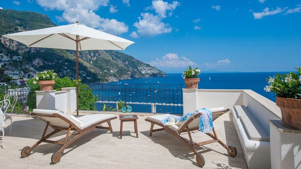 Une terrasse avec des chaises longues, un parasol blanc et des plantes en pot.