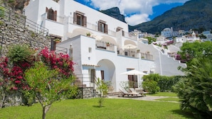 Un bâtiment blanc doté de balcons, d’un mur en pierre et d’un jardin avec un banc et des chaises.