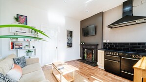 Ett modernt vardagsrum med en soffa, ett soffbord och en öppen spis. Det finns också ett köksområde med en spis och en ugn.