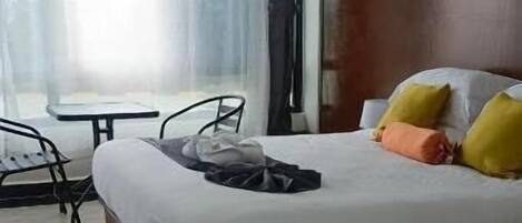 A hotel room with a large bed, a small table, and a chair.