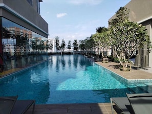 Una piscina rettangolare con acqua cristallina, circondata da un solarium in legno e alberi.