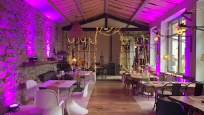 A restaurant with wooden tables and chairs, stone walls, and string lights. - Nature Cathare (Léran)