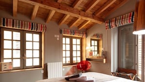 A bedroom with a wooden ceiling, large windows with striped valances, a red chair, and a bed with a white and brown bedspread. - Nature Cathare (Léran)