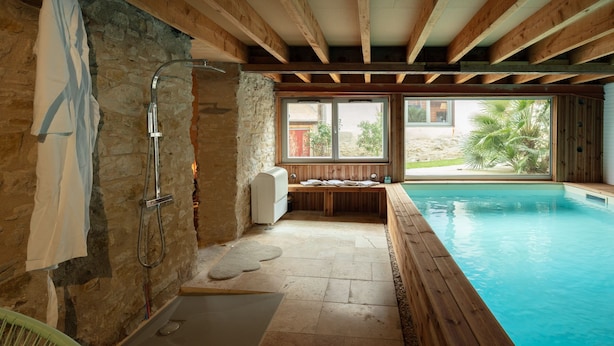 A spa area with a stone wall, wooden beams, a wooden deck, and a pool. - Nature Cathare (Léran)