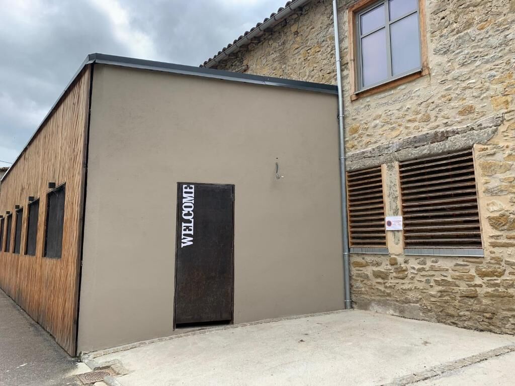 A building with a 'WELCOME' sign on the door, a stone wall, and a window with shutters.
