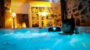 A person in a hot tub with a stone wall and a shelf with various items in the background. - Nature Cathare (Léran)