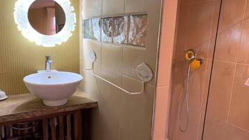 A bathroom with a white sink, a mirror with a decorative frame, and a shower area with a handheld showerhead.