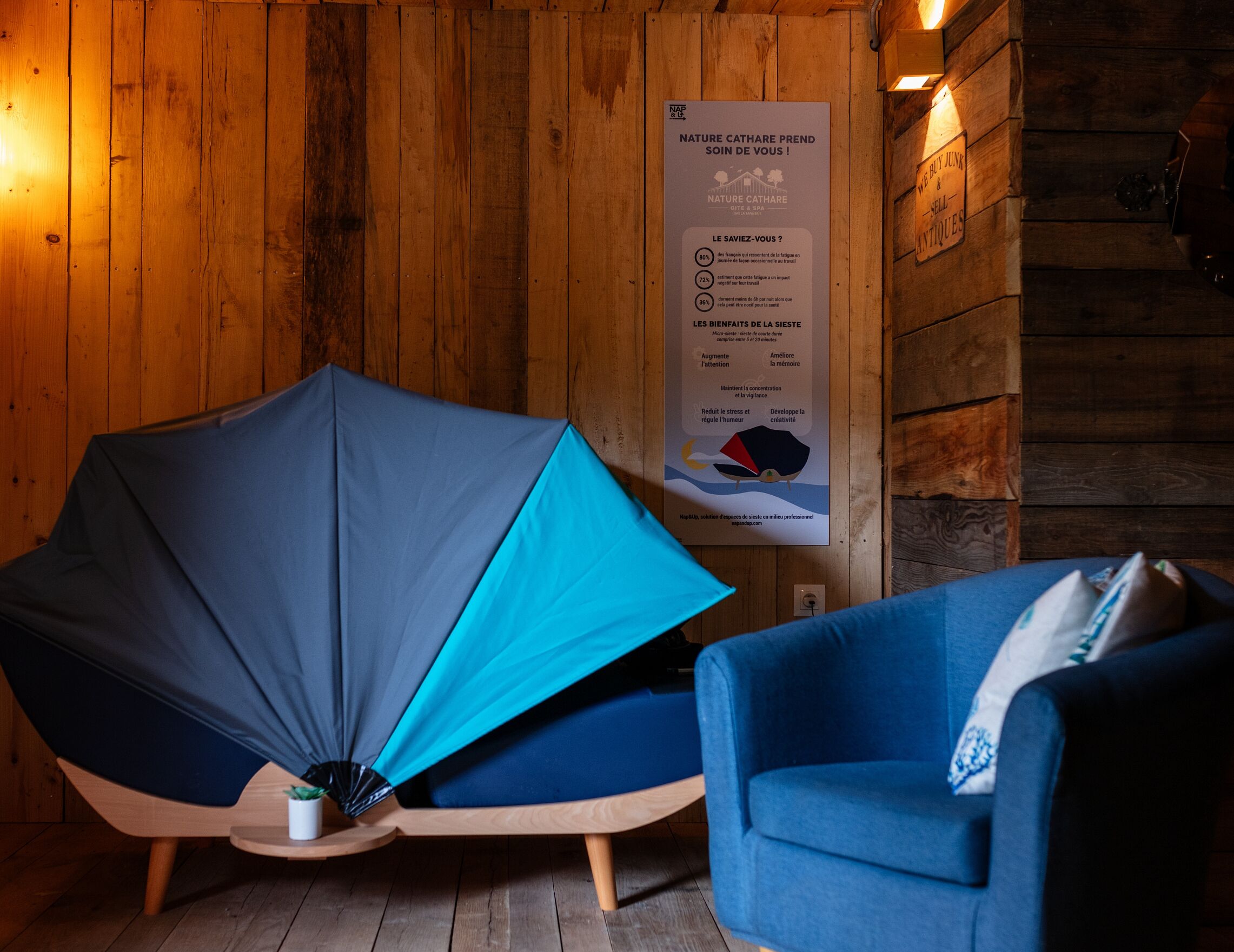 A room with a wooden wall, a blue chair, and a blue couch. There is a poster on the wall with text and a diagram.