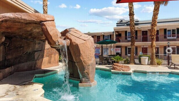 Una piscina con cascata, circondata da palme e un edificio con balconi.