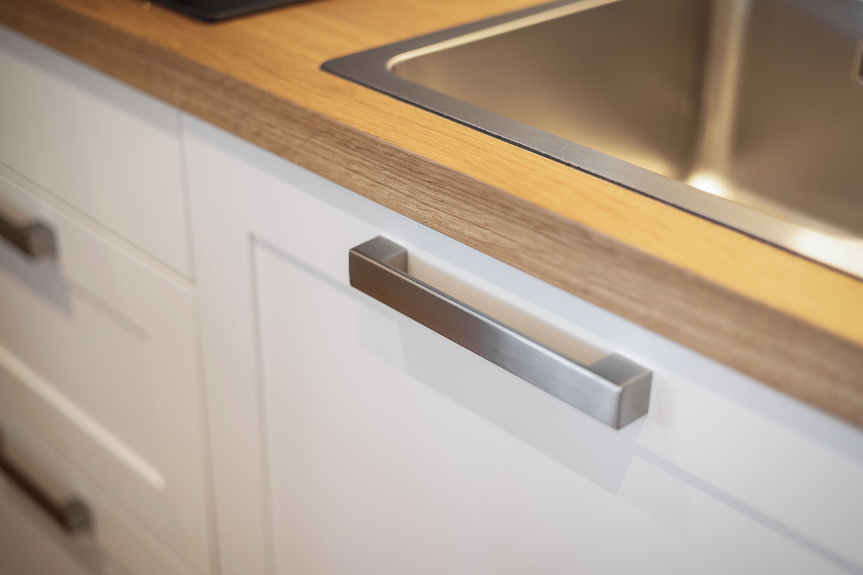 Una cocina con un lavamanos de acero inoxidable, encimera de madera y armarios blancos.