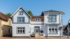 En tvåvåningsbyggnad med ett sadeltak, en central entré med en dörr och en liten veranda.