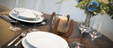 A dining table set with white plates, wine glasses, and cutlery. A candle holder with a lit candle is placed in the center.