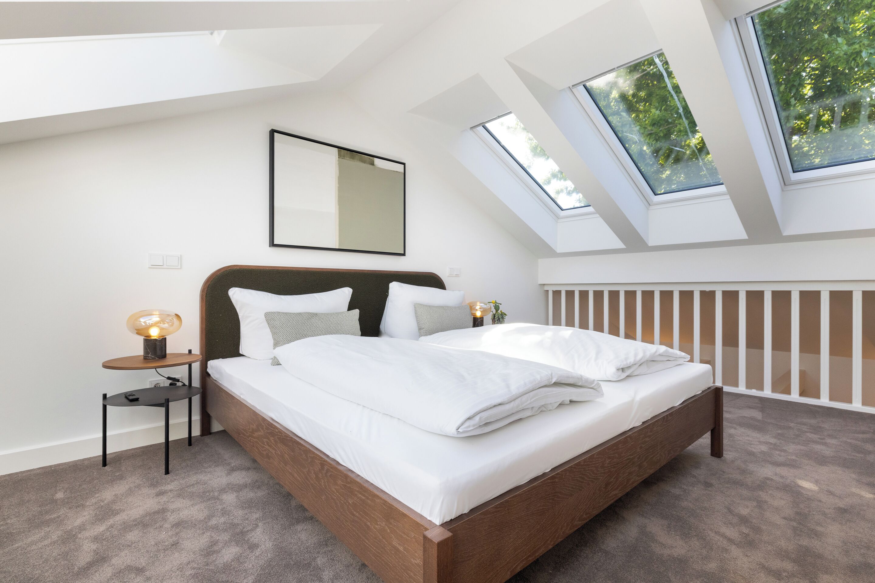 Ein Schlafzimmer mit Dachfenster, einem Bett mit weißer Bettwäsche, einem Nachttisch mit Lampe und einem gerahmten Bild an der Wand.