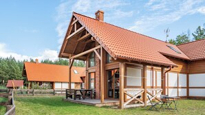 Puinen mökki, jossa on kalteva katto, suuret ikkunat ja terassi, jossa on ulkokalusteita.