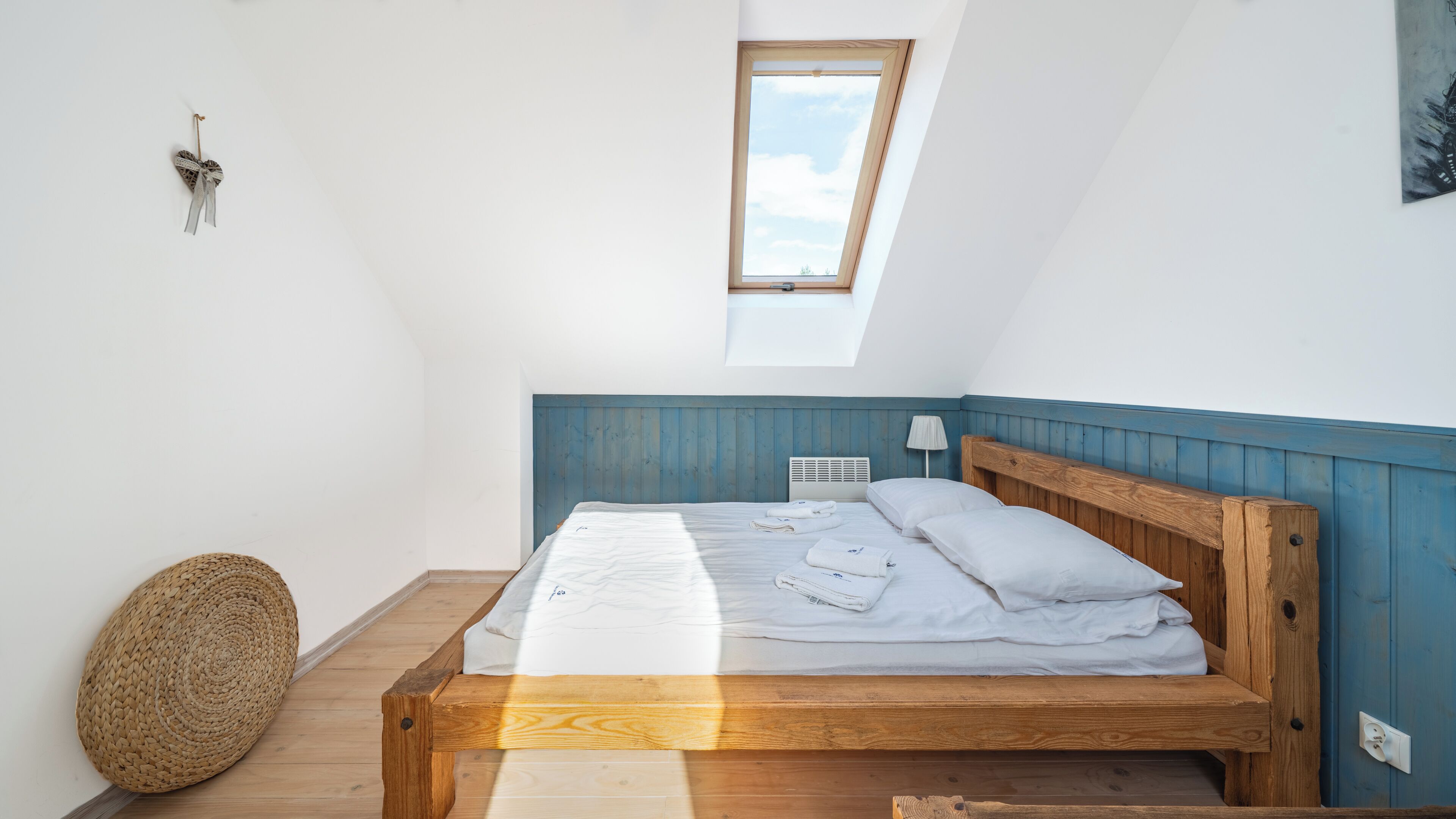 A bedroom with a sloped ceiling, a skylight, a wooden bed frame, and a woven basket.