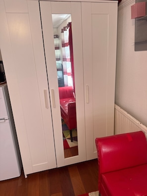 A room with a wardrobe, a red chair, and a kitchen area. - Room-charming London Guest Room With Gar (London)