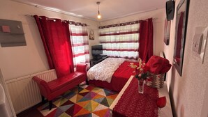 Une chambre à coucher avec un lit, un banc rouge, un tapis coloré et un téléviseur.