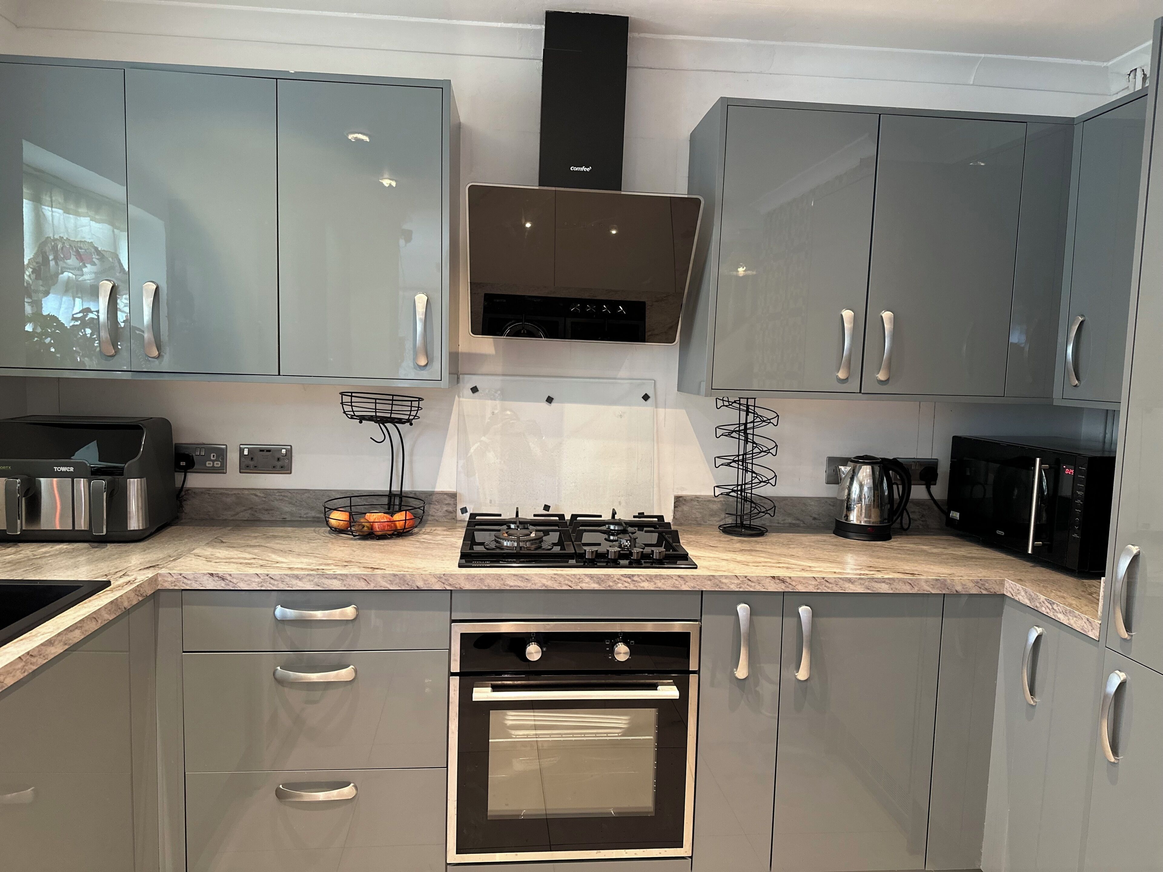 A modern kitchen with grey cabinets, stainless steel appliances, and a built-in oven.