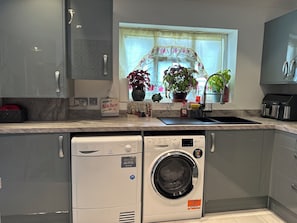 Ett modernt kök med gråa skåp, en inbyggd tvättmaskin och ett fönster med en blommig gardin.