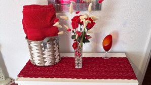 A white dresser with a red cloth on top, a woven basket, a vase with flowers, and a red wine glass. - Room-charming London Guest Room With Gar (London)