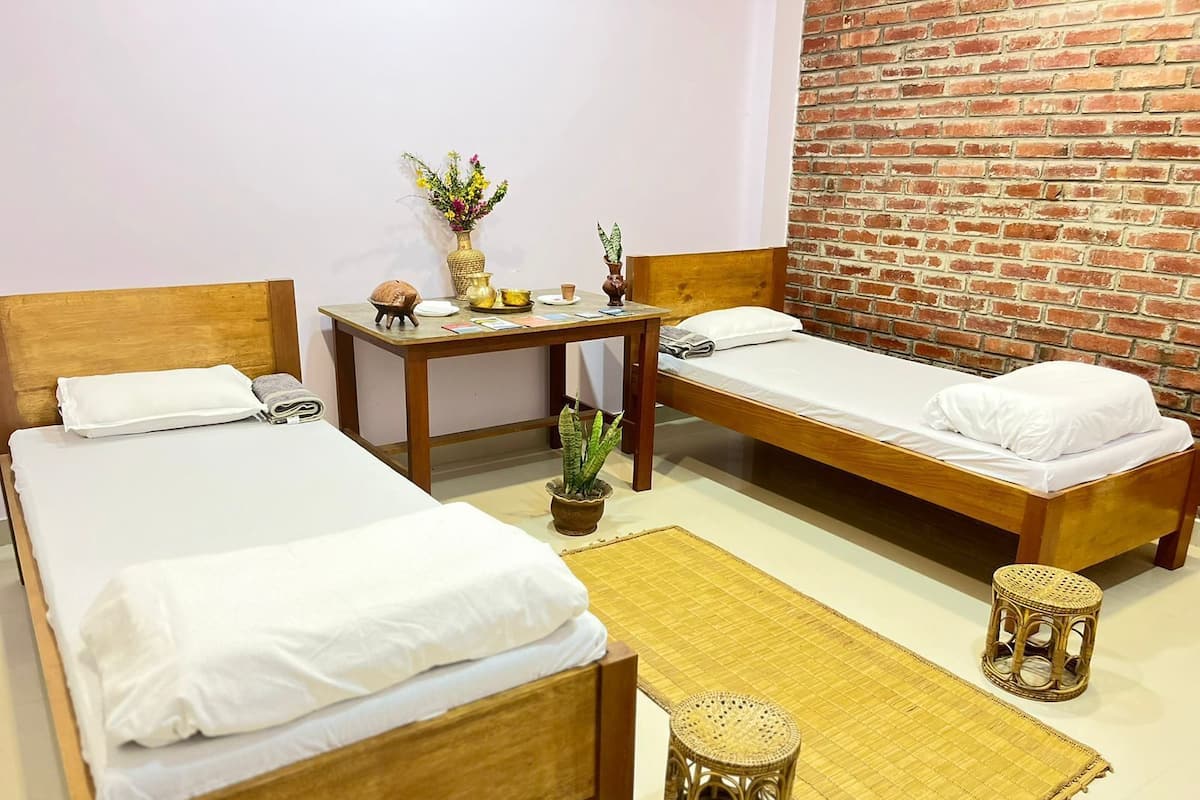 A room with two wooden beds, a small table with a vase of flowers, and a brick wall.