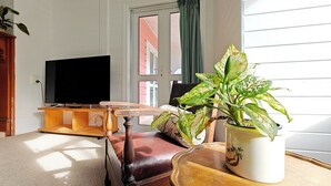 Ein Wohnzimmer mit Fernseher, einem Holzstuhl, einer Couch und einer Topfpflanze.