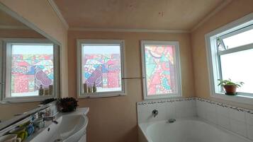 Een badkamer met een witte wastafel, een badkuip en twee ramen met glas-in-lood.