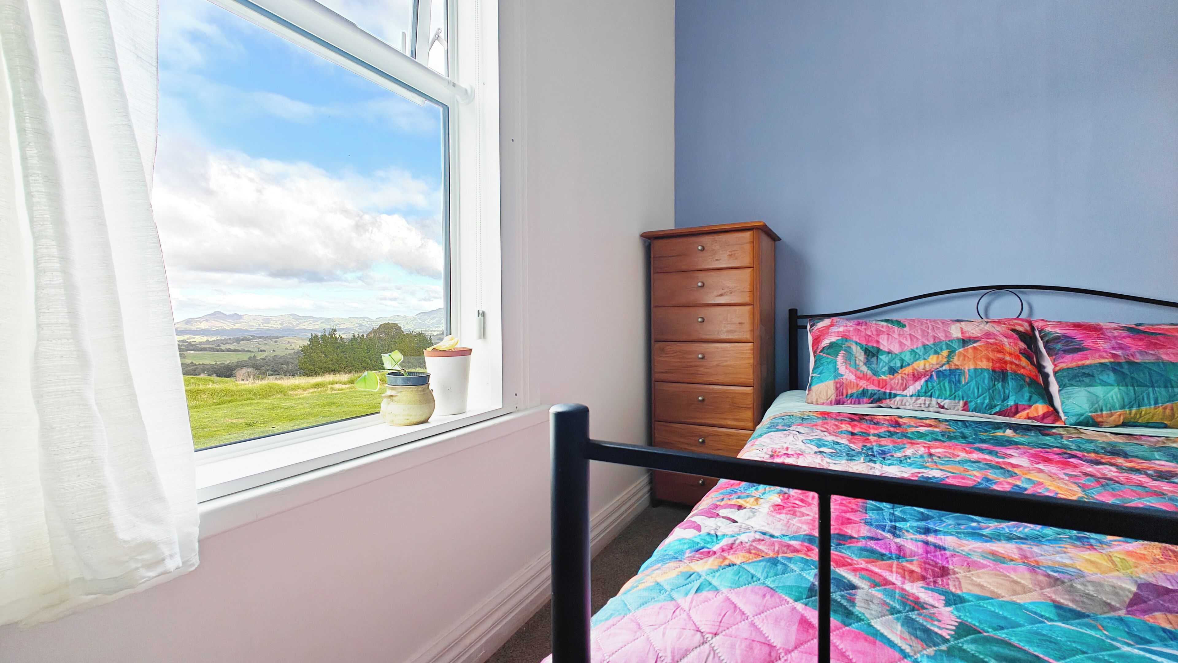 Ein Schlafzimmer mit einem Bett, einer Kommode und einem Fenster mit Blick auf eine Landschaft.