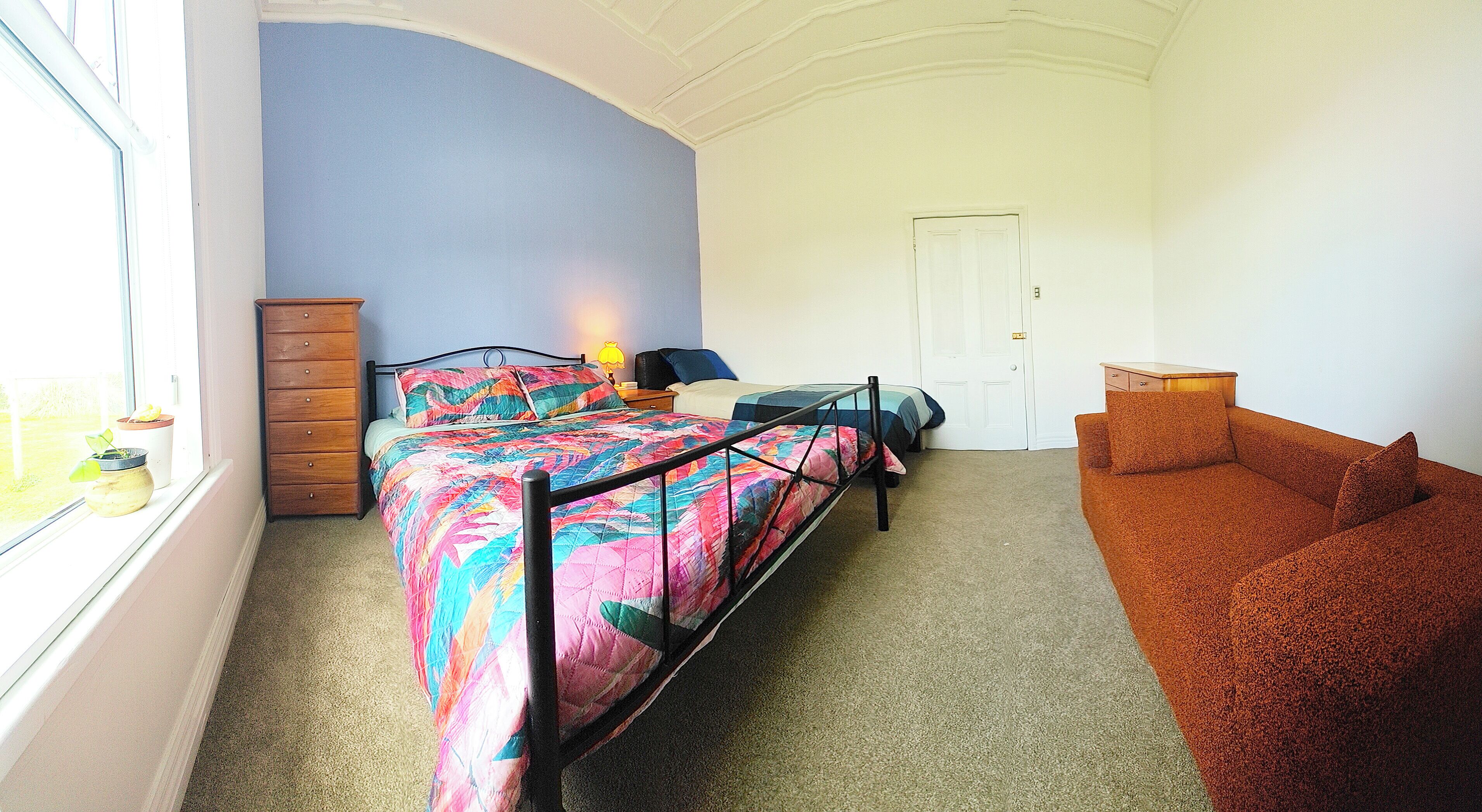 A bedroom with a bed, a dresser, a nightstand, a window, and a sofa.