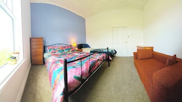 A bedroom with a bed, a dresser, a nightstand, a window, and a sofa.