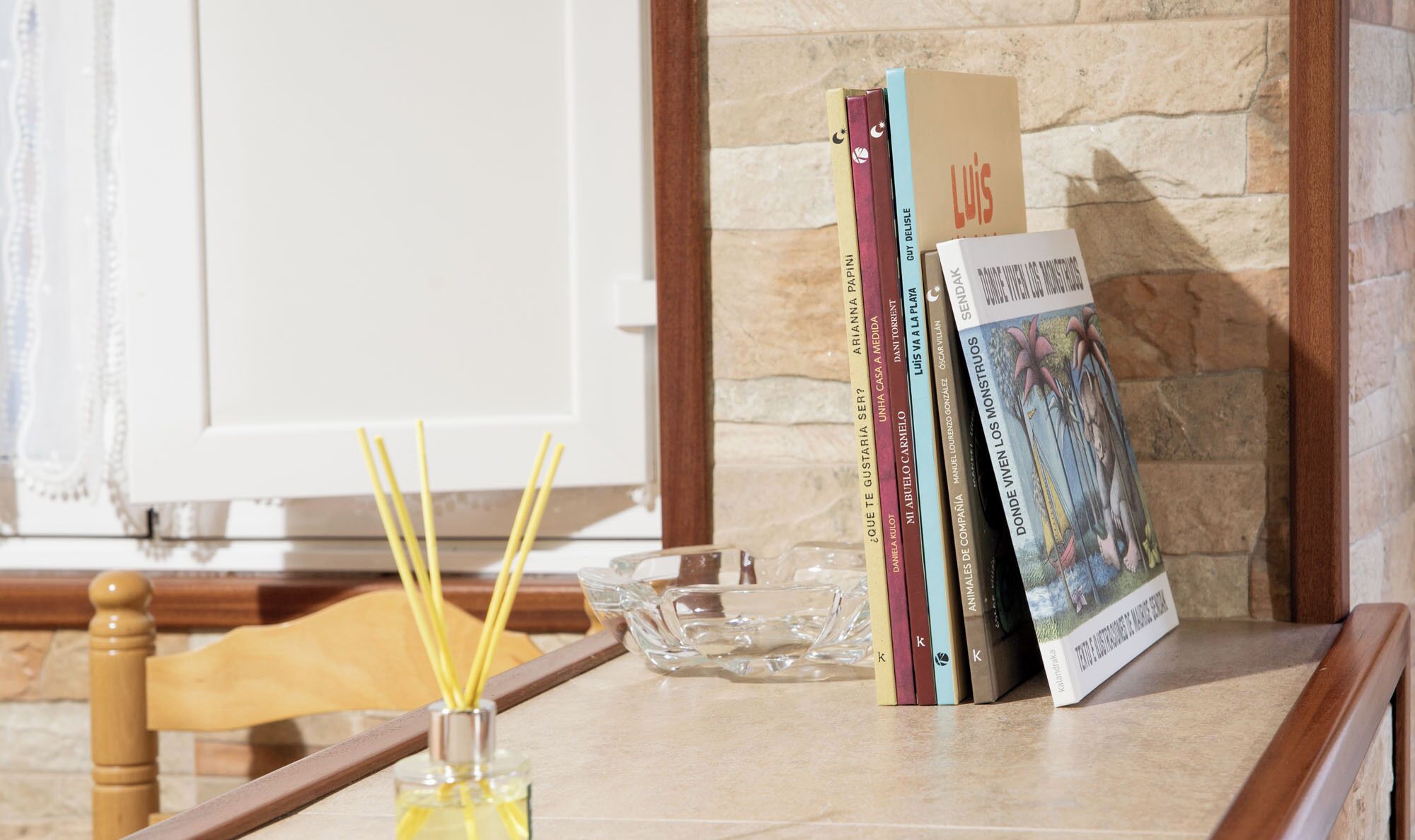 Une table avec des livres, un verre avec une bougie et une chaise en bois.