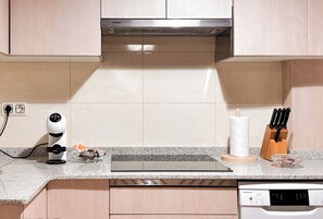 A modern kitchen with a built-in dishwasher, a kettle, and a knife block.