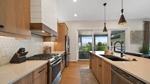 A modern kitchen with wooden cabinets, a stainless steel refrigerator, a gas stove, and pendant lighting. - 4BR Luxury Home, Hot Tub, Game Room, Walk to Pool & Grill (Boone)