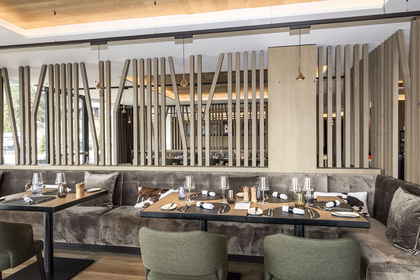 A modern restaurant with a long communal dining table, cushioned seating, and a wooden decorative partition.