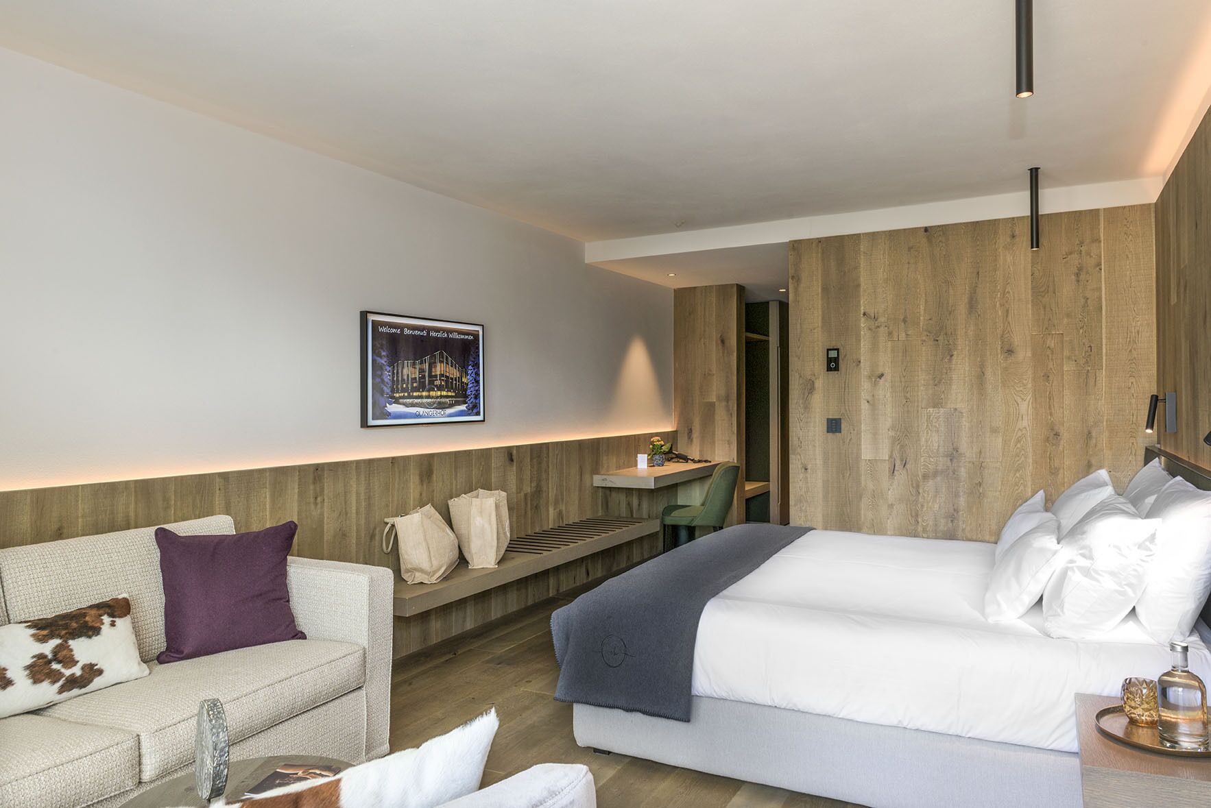 A modern hotel room with a large bed, a sofa, a desk, and a wooden accent wall.