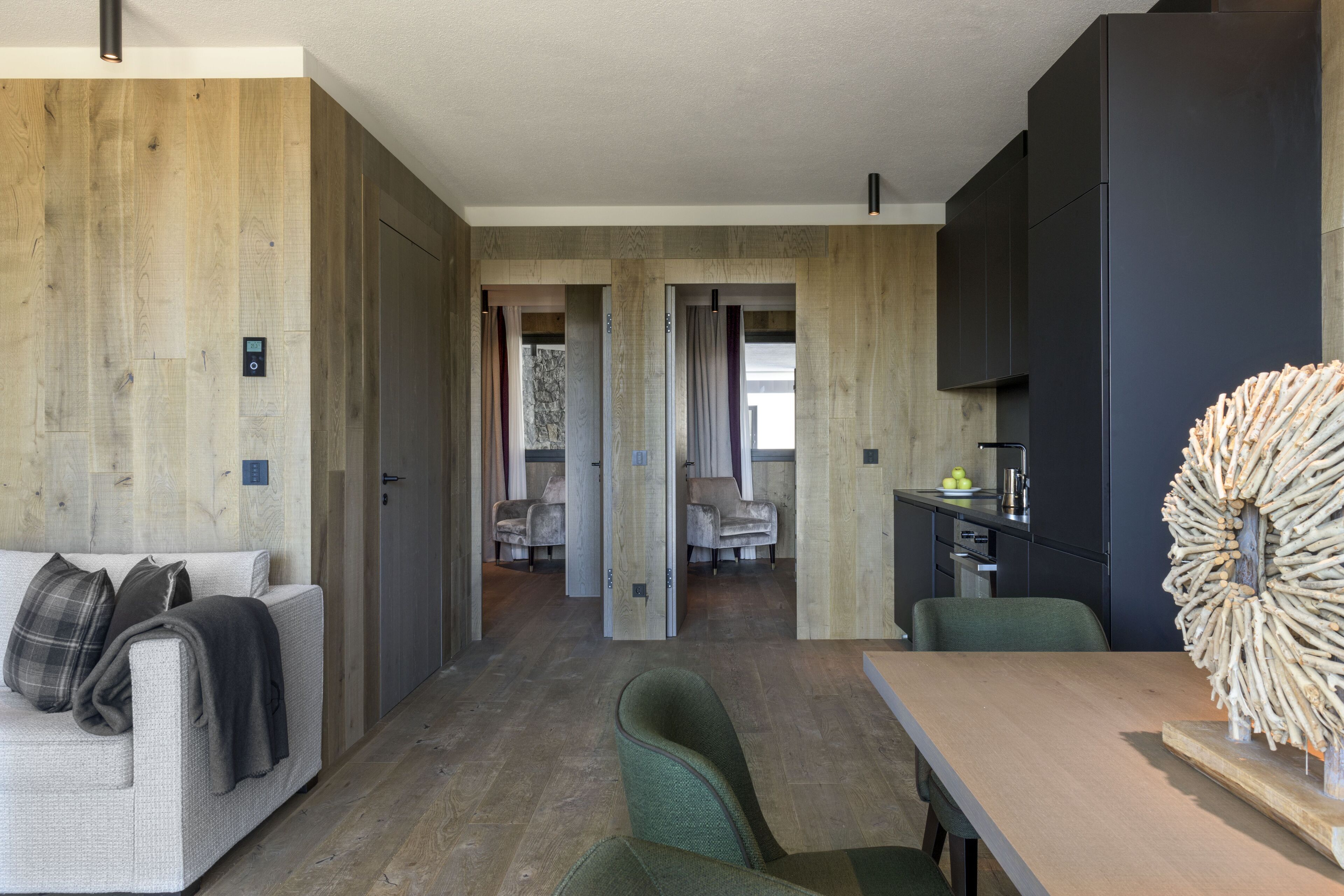 A modern interior with a wooden wall, a sofa, a dining table, and a kitchen area.