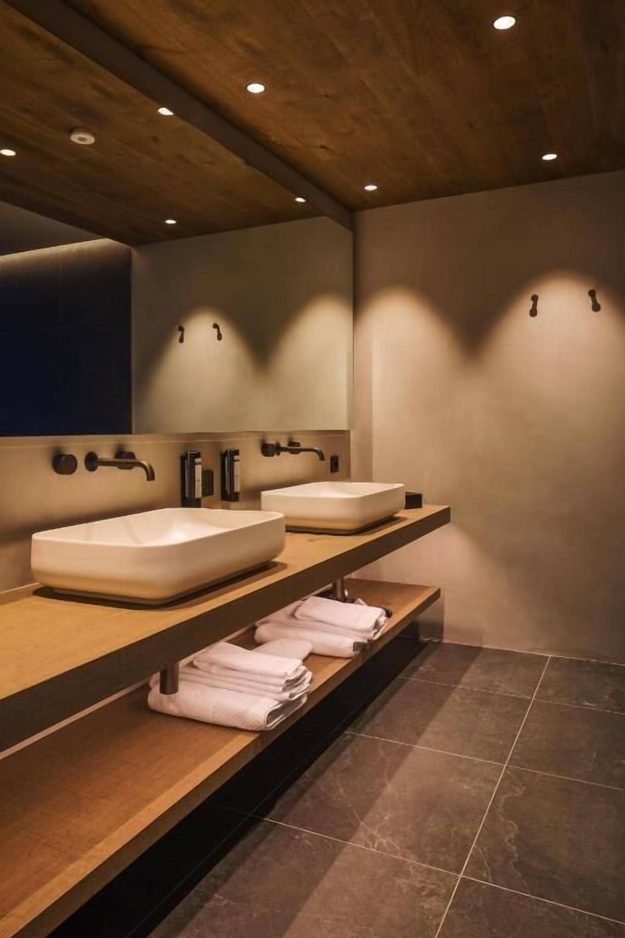 A modern bathroom with two sinks, wooden shelves, and a mirror.