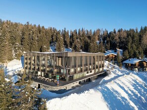 Un bâtiment moderne doté de grandes fenêtres et d’un balcon, entouré de neige et d’arbres.
