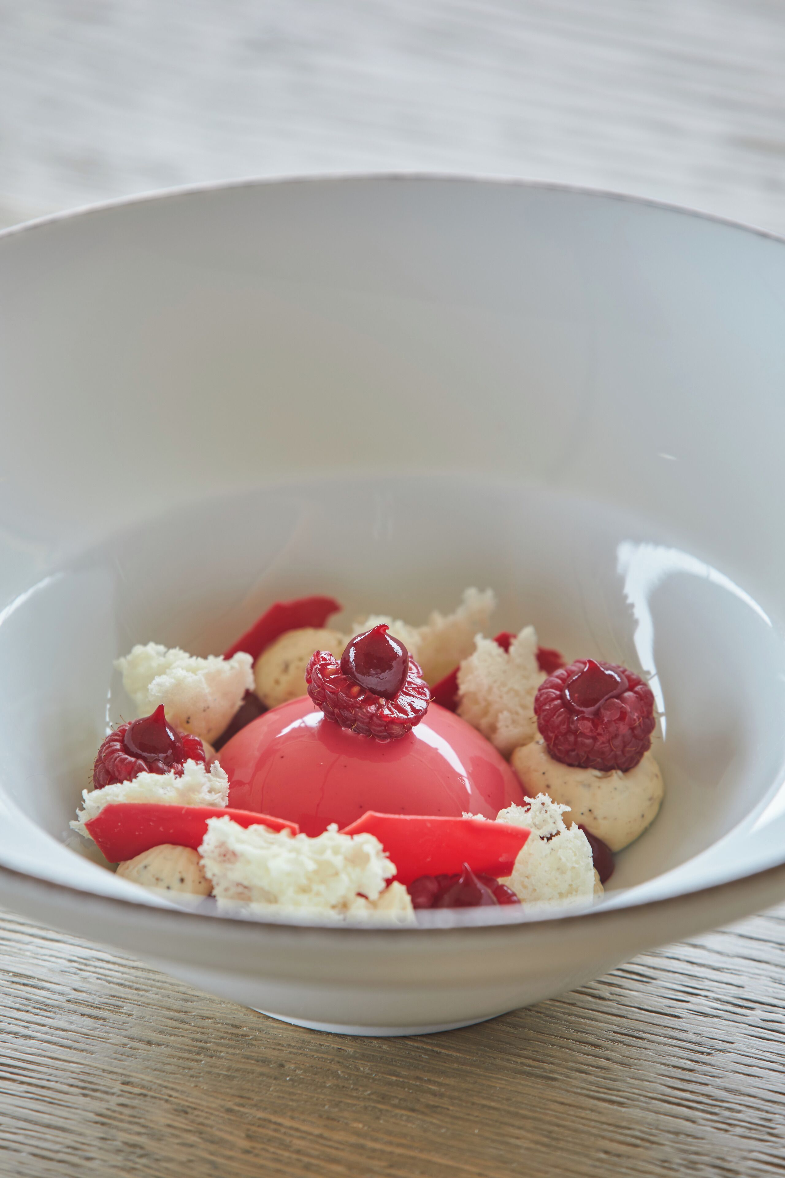 Un dessert servi dans un bol blanc, garni de framboises et d’une sauce rouge.