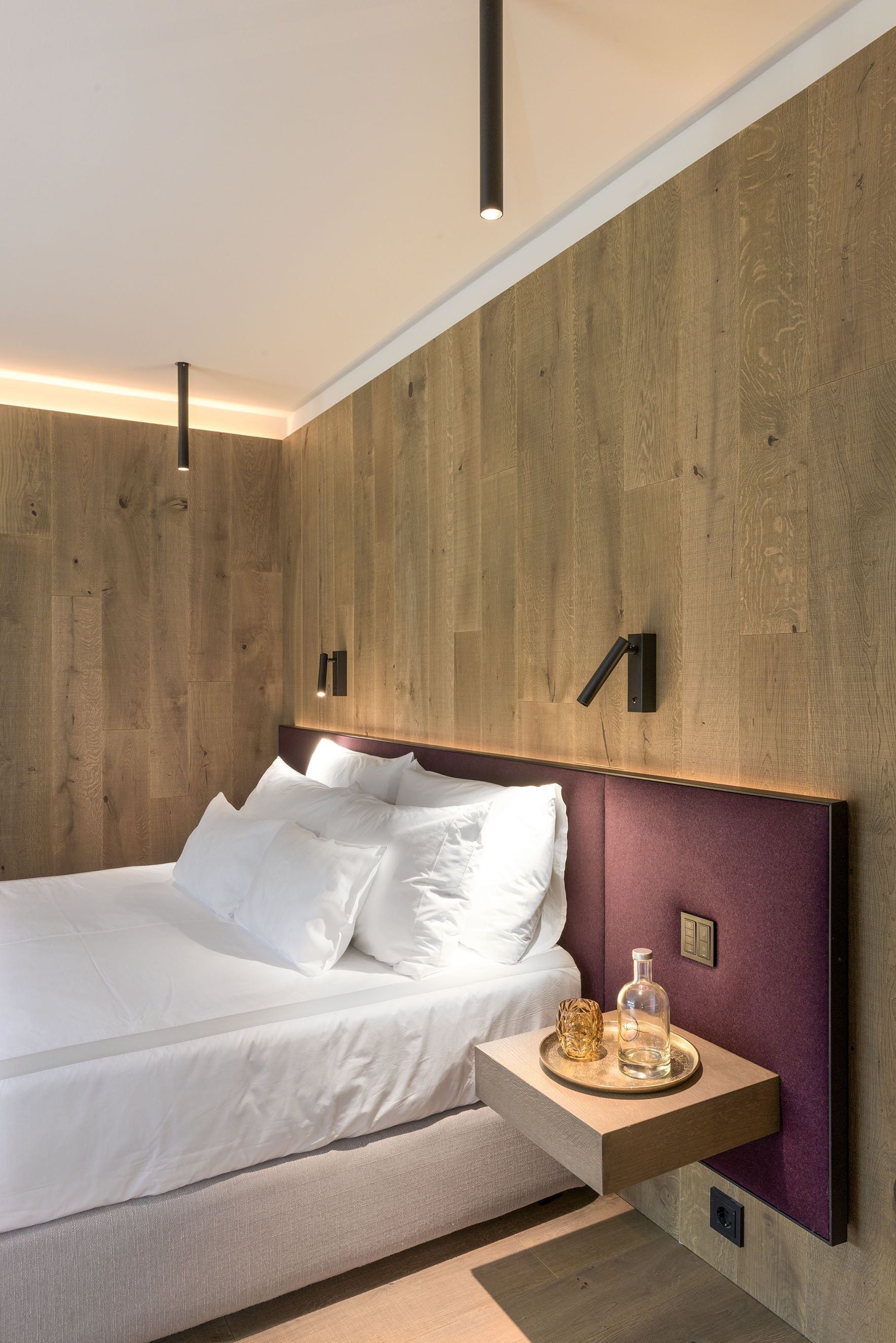 Une chambre à coucher moderne avec une tête de lit en bois, une table de chevet dotée d’un plateau et une petite table de nuit.