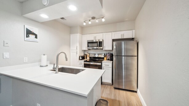 A modern kitchen with white cabinetry, stainless steel appliances, and a central island with a sink. - The Chandler 721 I Comfy 2 bed 2 Bath (Grand Praire)