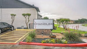 A Chandler Apartment Homes sign with a parking lot and landscaped area. - The Chandler 721 I Comfy 2 bed 2 Bath (Grand Praire)