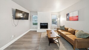 A living room with a flat-screen TV, a fireplace, a sofa, and a coffee table. - The Chandler 721 I Comfy 2 bed 2 Bath (Grand Praire)
