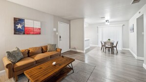 A modern living room with a brown leather sofa, a wooden coffee table, and a dining area with a white table and chairs. - The Chandler 721 I Comfy 2 bed 2 Bath (Grand Praire)