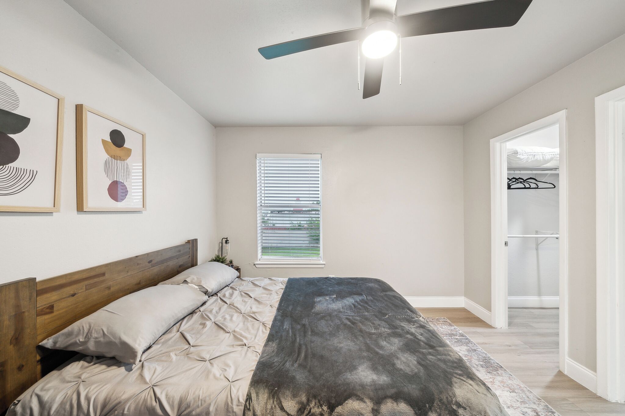 A bedroom with a bed, a ceiling fan, a window with blinds, and a door leading to a closet.