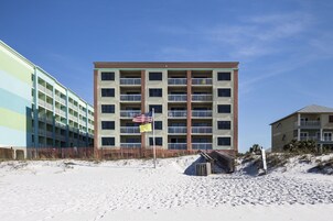 Un hotel de varios pisos con balcones, situado en una playa arenosa bajo un cielo despejado.