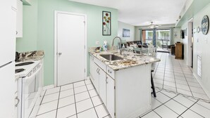 A kitchen with white cabinets, a sink, and a stove. There is a door leading to another room. - Harbour Place 206 (Orange Beach)