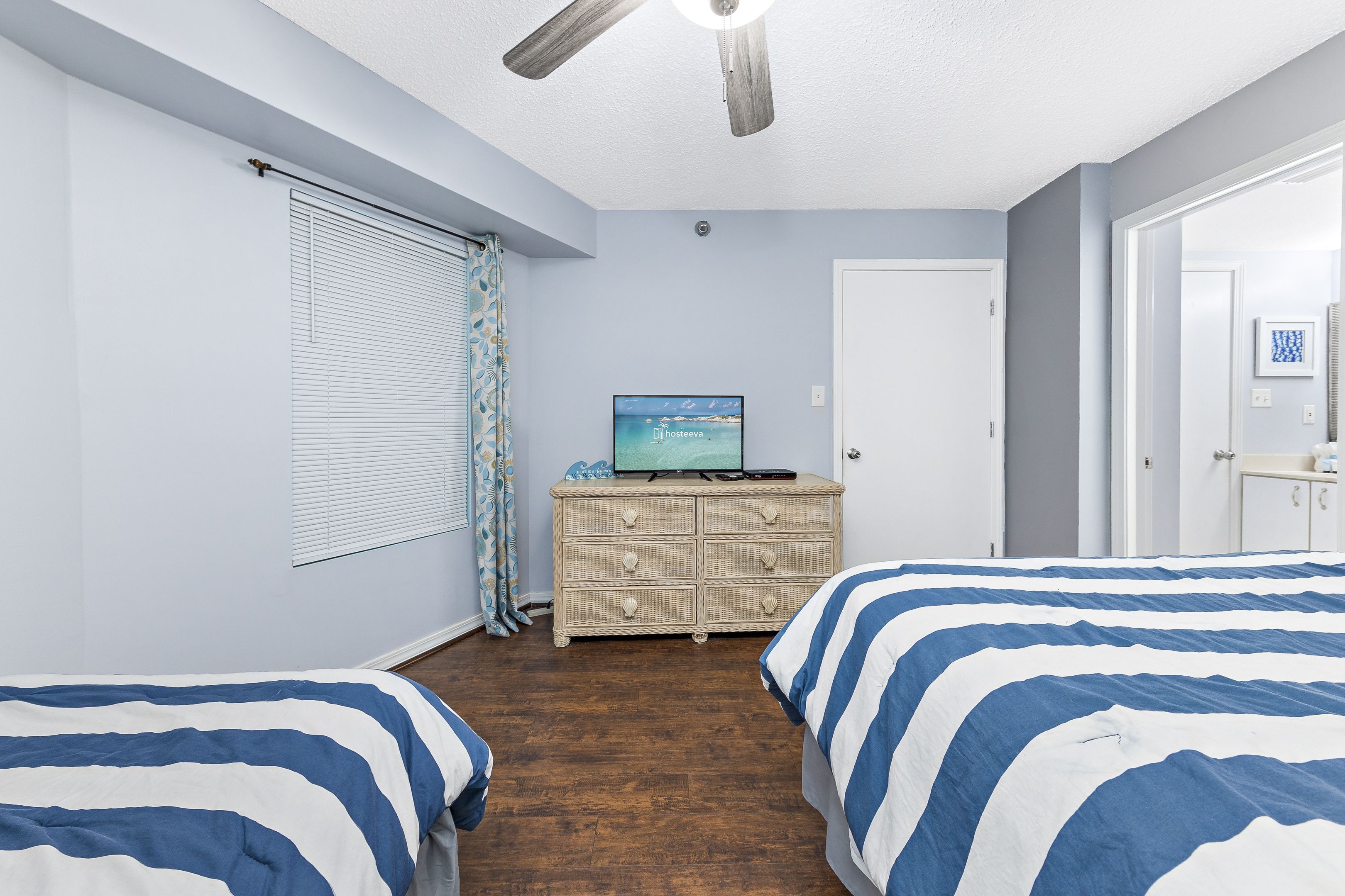Een slaapkamer met twee bedden, een televisie op een dressoir en een plafondventilator.